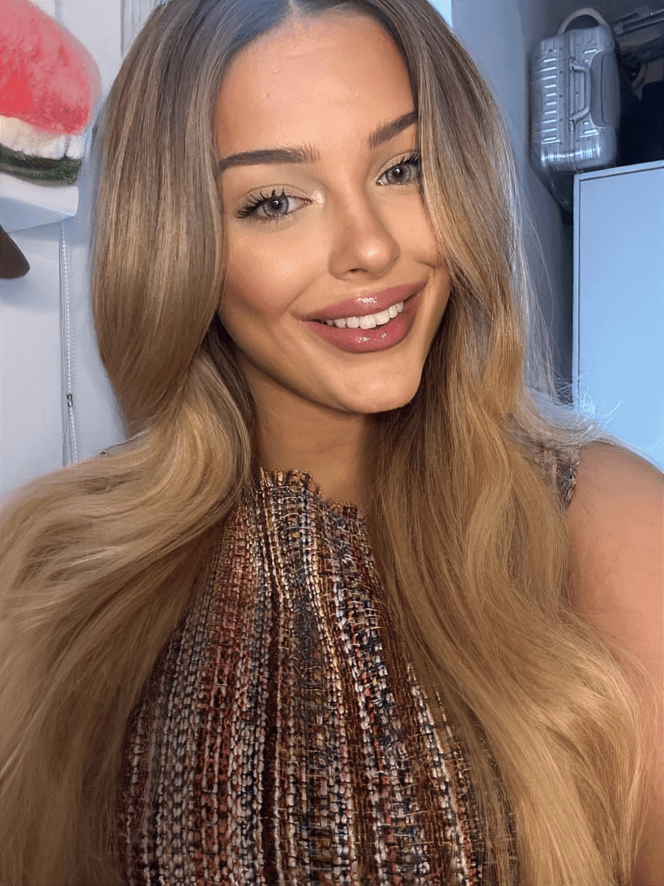 Smiling woman with long blonde hair and light eyes wearing a textured, multicolored top.